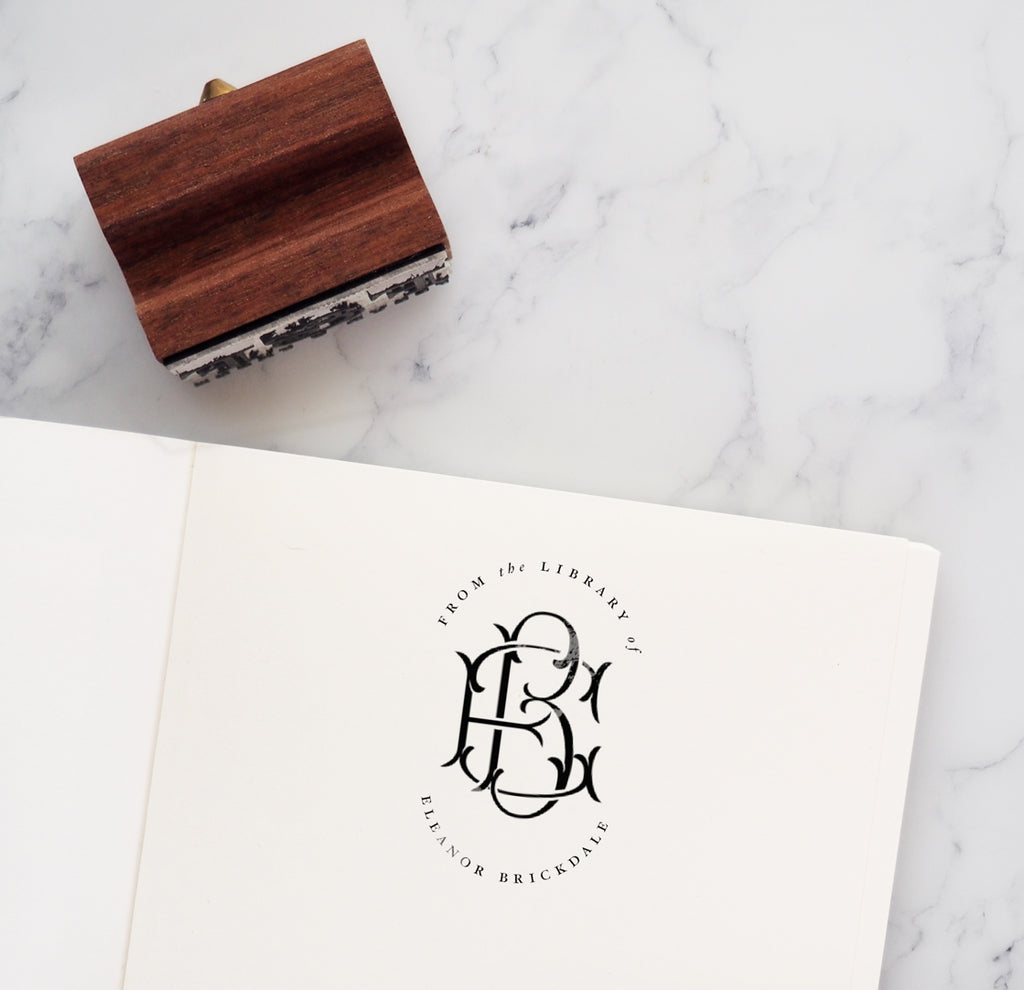Personalised 'From the library of...' bookplate stamp in book next to wooden rubber stamp