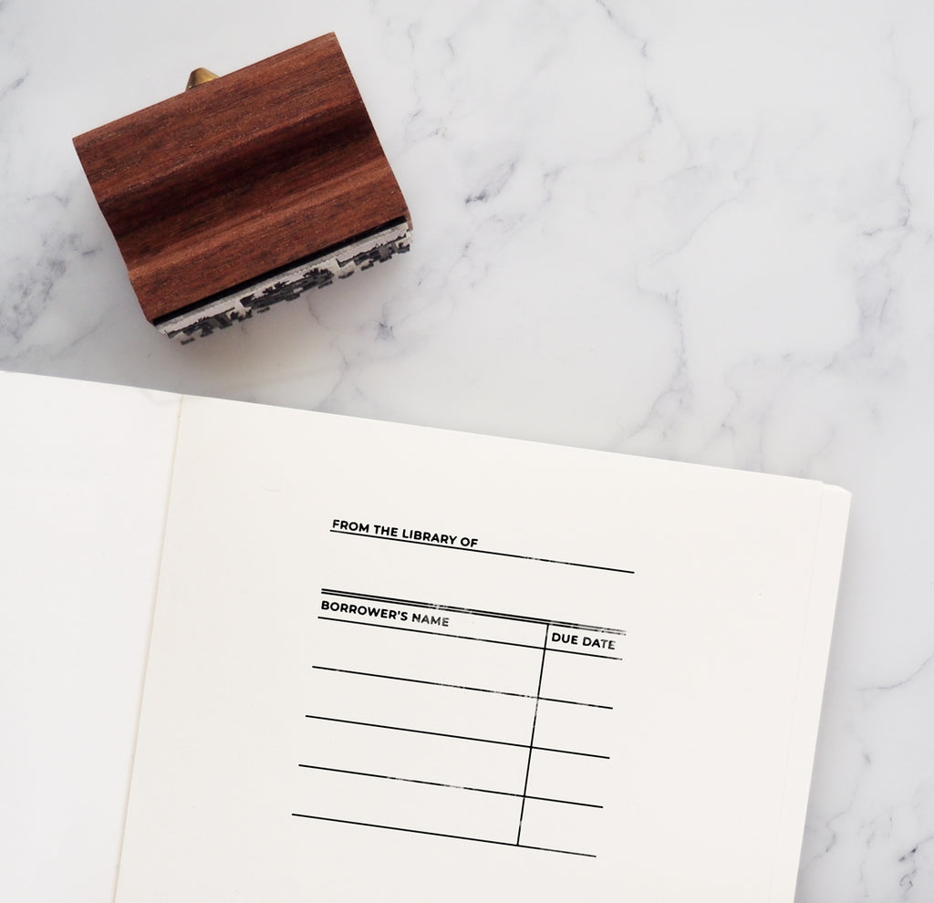 Library card bookplate stamp in book next to wooden rubber stamp