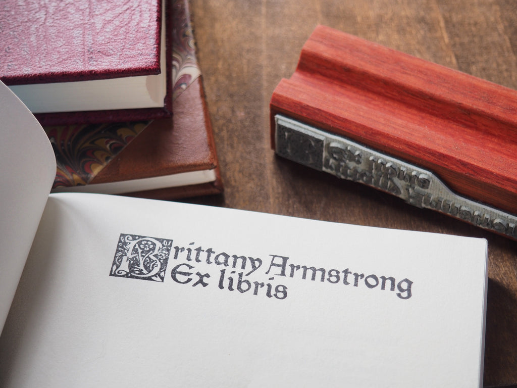 Personalised ex libris bookplate stamp in book next to stack of books and wooden rubber stamp