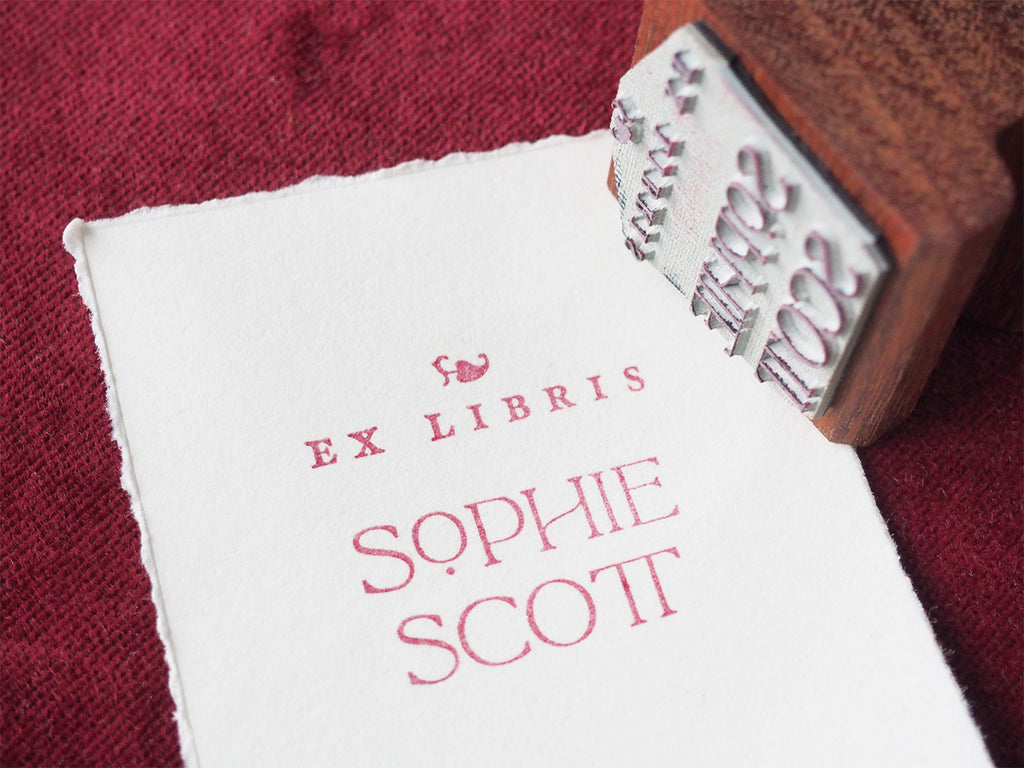 Personalised ex libris bookplate stamp on paper next to wooden rubber stamp