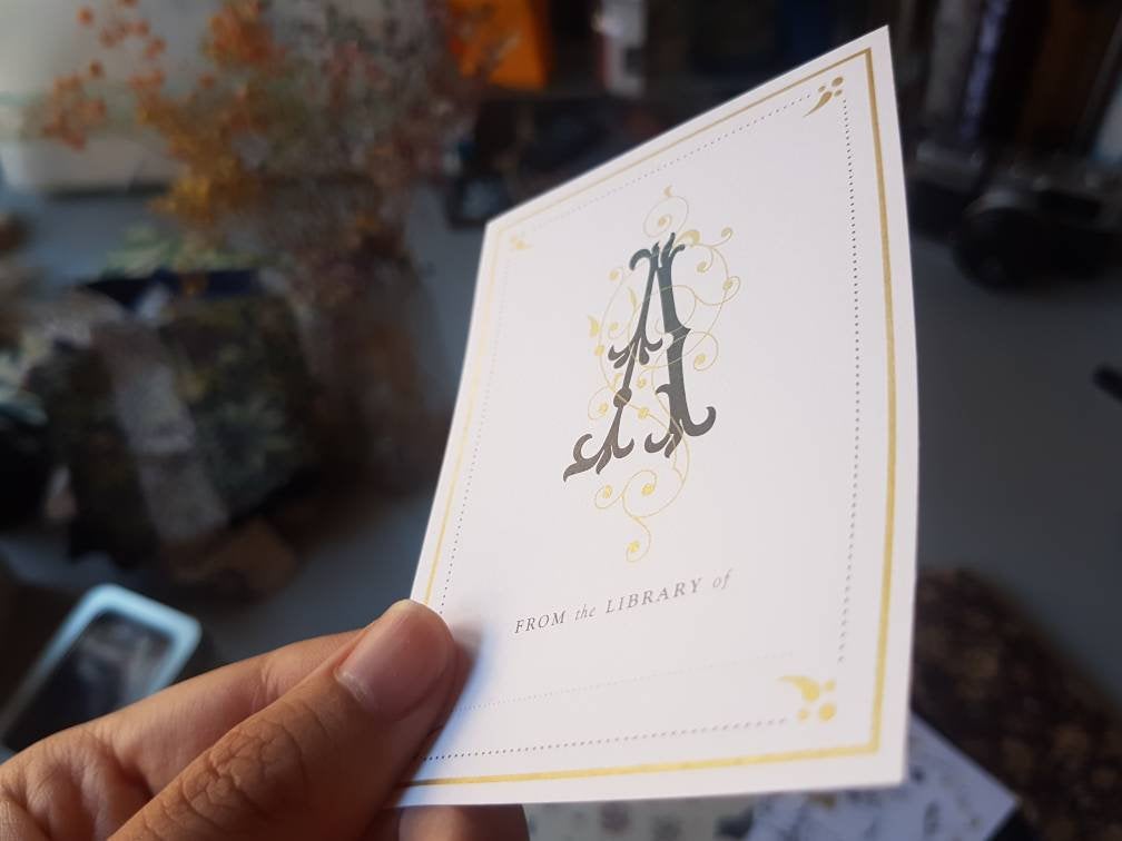 Hand holding a monogram initial bookplate sticker label at an angle 