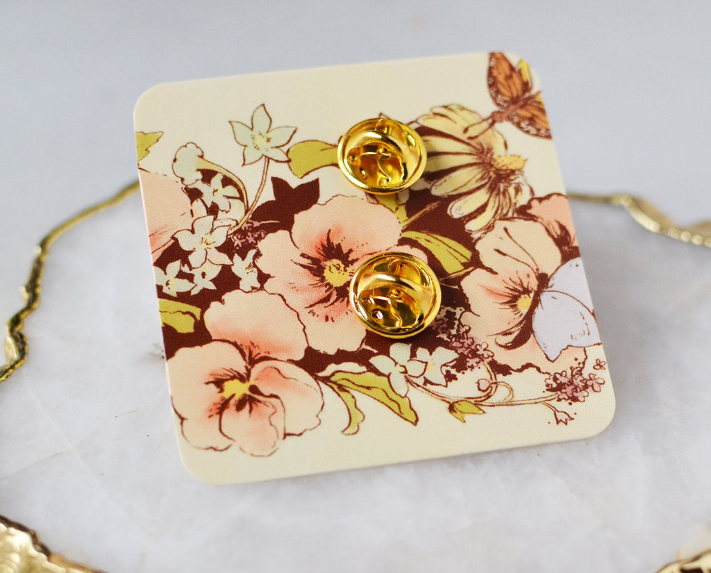 Reverse side of Victorian floral enamel pin secured to backing card showing butterfly catch pins